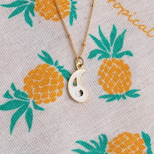 Gold plated copper necklace featuring a white enamel Yin Yang pendant on tropical fabric