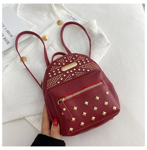 Detail view of red mini backpack with golden studs, pearls, and front zipper pocket