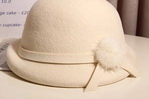 Detail of cream wool beret with soft fur pom-poms and matching ribbon accent