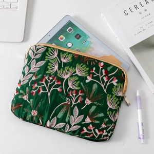 Detail of green floral quilted laptop sleeve with golden zipper on a modern office desk