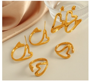 Macro view of gold plated hollow heart earrings and adjustable rings on silk fabric