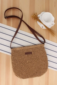 Detail of woven straw shoulder bag with adjustable brown leather strap on wooden surface