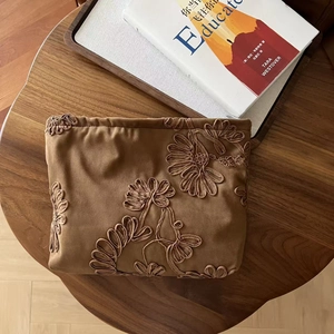 Detailed embroidery of daisies on a vintage camel suede cosmetic bag with wood background