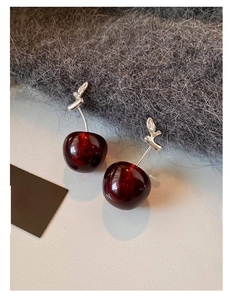 Macro view of dark red resin cherry earrings with detailed silver leaf hooks and glossy finish