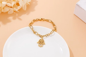Close-up of golden stainless steel Hamsa hand bracelet on white ceramic plate