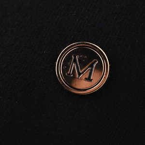 Macro shot of rose gold M metal badge on black fabric texture of a baseball cap