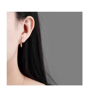 Close-up of a minimalist gold lightning bolt earring worn by a model on a grey background