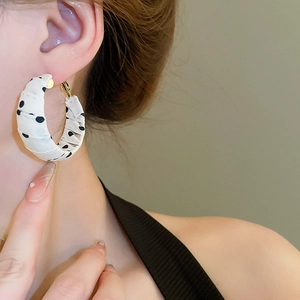 Close-up of a model wearing C-shaped polka dot fabric wrapped hoop earrings in retro style