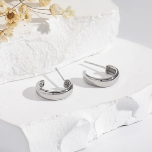 Minimalist silver C-shaped hoop earrings for men and women on a white stone base