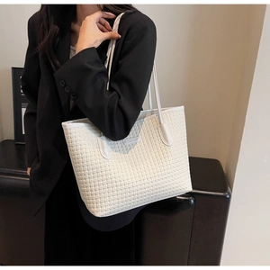 Detail view of a white woven tote bag with a soft texture on a black blazer model