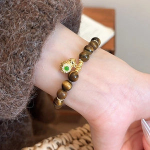 Close-up of tiger eye bead bracelet with hollow gold gourd charm and green gemstone