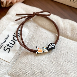 Detail of cute calico cat and fishbone charms on a brown elastic hair tie band