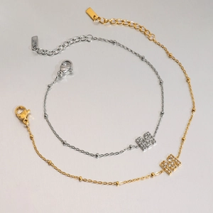 Close-up of gold and silver M-letter pendant bracelets with zircon stones and lobster clasp