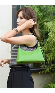 Model wearing a glossy green underarm bag against a nature background outdoors
