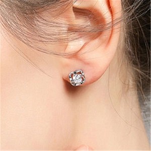 Close-up of a silver floral stud earring with a central clear zircon on a model ear