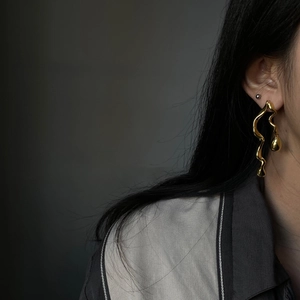 Minimalist gold wave drop earrings featuring fluid liquid metal design on model