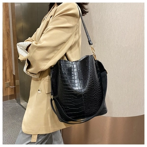 Detail of black crocodile texture tote bag with wide strap and gold hardware on model