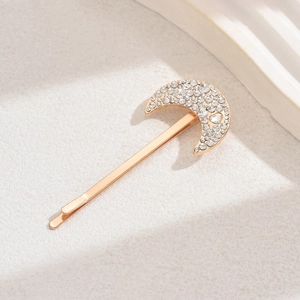Elegant gold crescent moon hair clip with sparkling rhinestones on a beige surface