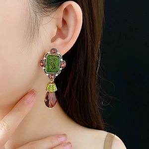 Close-up of vintage gold earrings with green gemstones and brown teardrop pendants