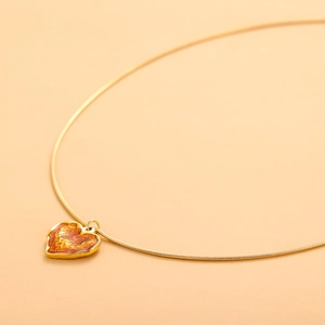 Minimalist gold heart pendant necklace with marble texture on a warm pastel background