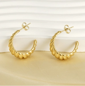 Detailed close-up of 18K gold stainless steel twisted hoop earrings on soft fabric
