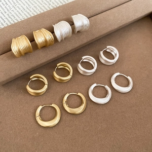 Detailed display of brushed metal stud earrings and hoops on a brown textured tray