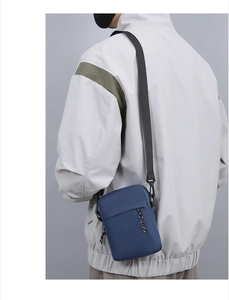Detail of blue nylon crossbody bag with black woven strap and zipper cord accents