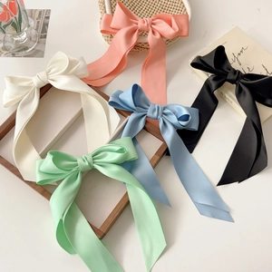 Flat lay of large satin bow hair clips in pink, cream, black, blue and green on a white surface