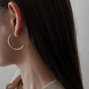 Close-up of minimalist golden large hoop earring with a matte textured spiral design