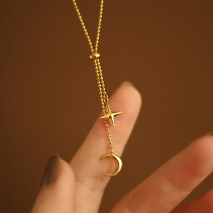 Macro detail of gold star and crescent moon pendants on a delicate beaded chain necklace