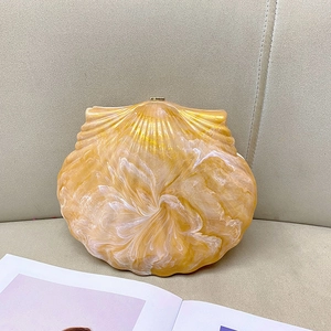 Détail de la pochette de soirée en forme de coquille en résine ambre et crème marbrée