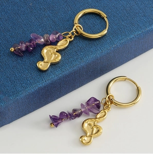 Close-up of 18k gold-plated earrings featuring natural purple stones and musical note charms