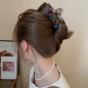 Detail view of a large brown acrylic hair claw clip with colorful beads on a bun