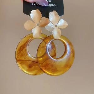 Close-up of golden flower stud with amber resin hoop earring held in hand
