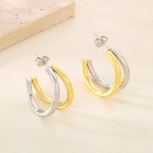 Gros plan de boucles d'oreilles en C bicolores or et argent en acier inoxydable sur texture