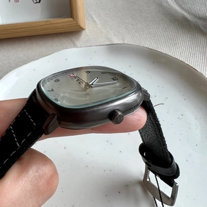 Close-up of a square grey watch with silver dial and black leather strap held by hand