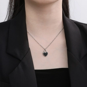 Close-up of a silver chain necklace with a black heart-shaped locket and bead details
