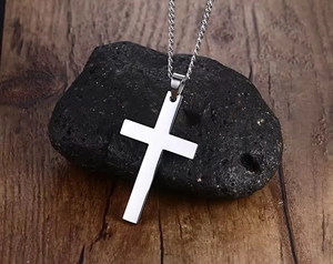 Close-up of polished silver stainless steel cross pendant on textured black rock