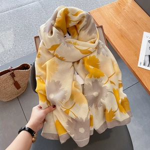 Detail of soft yellow and beige floral cotton linen scarf styled with a straw bag