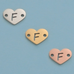Macro detail of heart pendants with letter F in silver, gold and rose gold mirror finish