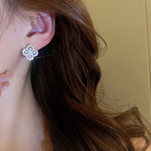Macro shot of a sparkling silver four-leaf clover stud earring worn on a model's ear