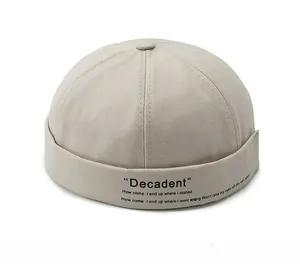 Detail of beige cotton brimless docker cap featuring black decadent typography and six-panel crown