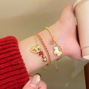 Close-up of stacked red cord and gold bracelets with horse and bell charms on wrist