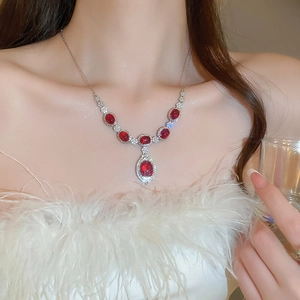 Detailed close-up of a silver necklace with oval red gemstones and zircon floral accents