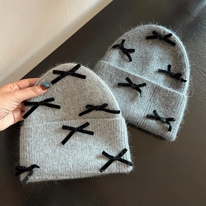 Detailed top view of grey velvet bow knit beanies on a wooden table surface