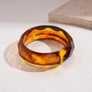 Macro shot of geometric acrylic bangle with amber swirl pattern and faceted surface