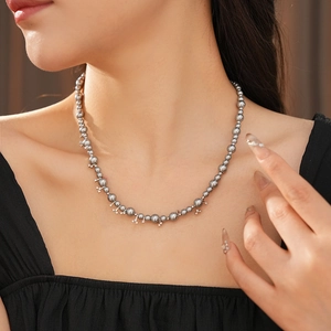 Close-up of grey pearl necklace with metallic cross accents on a female model