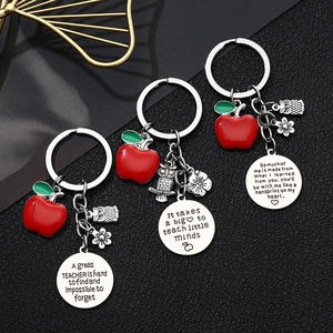 Three engraved stainless steel teacher keychains with apple and owl charms on dark background
