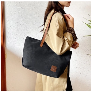 Detail of black canvas tote bag with brown leather straps and branded logo patch