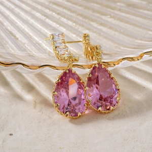 Elegant gold drop earrings with pink water-drop crystals on a glass display tray